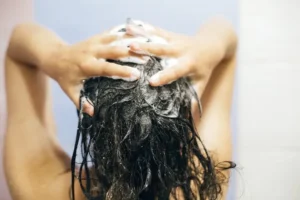 Jovem mulher lavando o cabelo com xampu, mãos com espuma em close-up