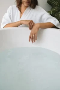 uma mulher em um roupão de banho apoiando-se em uma banheira